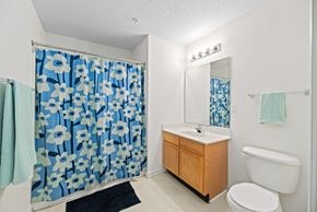 Farmville apartment for rent - A bathroom with a white toilet, a sink, a mirror, and a shower curtain with blue flowers.