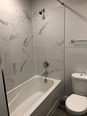 Halifax apartment for rent - A white toilet sits next to a bathtub in a bathroom with marble tile walls.