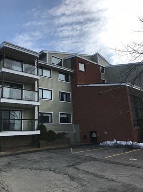 Halifax apartment for rent - A building with a grey and red facade is surrounded by a parking lot.
