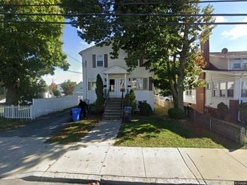 Cranston apartment for rent - A white house with a blue trash can in front of it.