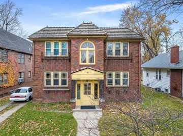 Rockford apartment for rent - A two-story brick house with a yellow front door and a car parked in front.