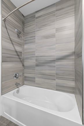 Newark apartment for rent - A white bathtub with a shower head and a wall of tiles.