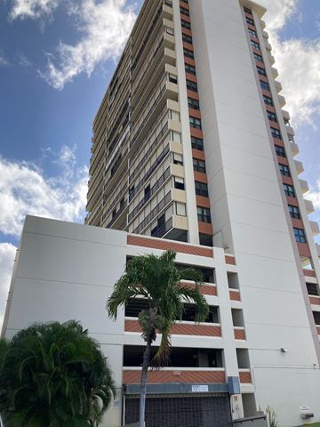 Honolulu apartment for rent - A tall white building with a palm tree in front of it.