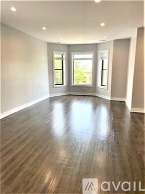 Chicago apartment for rent - A spacious room with wooden flooring and two windows.