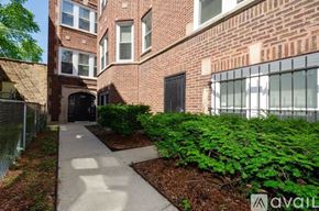 Chicago apartment for rent - A brick building with a fence and bushes in front.
