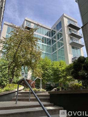 Columbus condo for rent - A modern building with glass windows and balconies is surrounded by trees and greenery.
