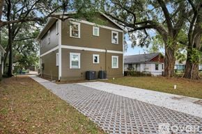 Tampa apartment for rent - A two-story house with a brown and beige exterior is surrounded by trees and has a brick driveway.