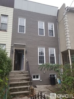 Brooklyn apartment for rent - A grey house with a black trash bin in front.