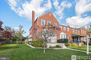 Towson house for rent - A large red brick house with a white fence and a tree in front.