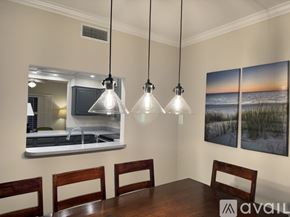 Atlantic Beach condo for rent - A dining room with a wooden table and chairs, a kitchen area with a sink and a mirror, and a painting of a beach scene on the wall.