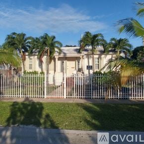 Coral Gables house for rent - A white house with a fence in front of it and palm trees in the background.