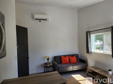 Los Angeles apartment for rent - A living room with a grey couch, a small table with flowers, and a window with a view of trees.