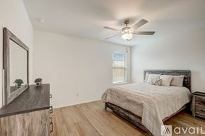 Mckinney house for rent - A bedroom with a large bed, a ceiling fan, and a wooden dresser.