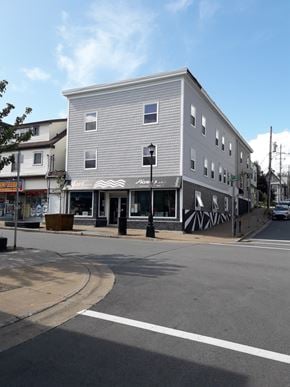Dartmouth apartment for rent - A grey building with a black and white striped awning sits on a street corner.