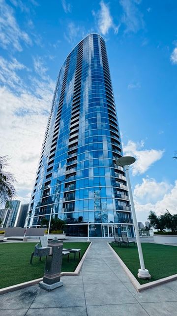 Honolulu apartment for rent - A tall, modern glass building stands under a blue sky.