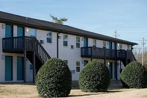 Huntsville apartment for rent - A building with a balcony and two bushes in front.