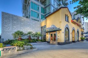 Vancouver apartment for rent - A building with a yellow facade and a sign that reads "CANDORA" is surrounded by a white lattice fence and greenery.