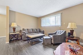 Iowa City apartment for rent - A living room with a grey couch, a grey armchair, a grey chair, a grey ottoman, a wooden coffee table, and two lamps.