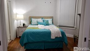 Tampa apartment for rent - A bed with a teal comforter and a white blanket is in the foreground of a room with a lamp and a nightstand.