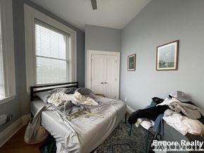 Boston apartment for rent - A bedroom with a bed in the center of the room with a grey bedspread and a chair with clothes on it.