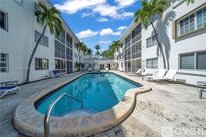 Key Biscayne apartment for rent - A swimming pool in the middle of a sandy area with palm trees and white buildings in the background.