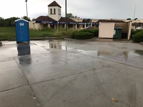 Olathe apartment for rent - A blue porta potty is in the foreground of a wet parking lot.