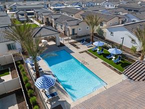 Phoenix apartment for rent - A swimming pool surrounded by white lounge chairs with blue cushions and blue and white striped umbrellas with a green area at Allero 59  Apartments, Phoenix, Arizona