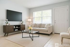 Miami Gardens apartment for rent - A living room with a grey rug, a white sofa, a wooden cabinet, a flat screen TV and a door.