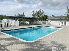Miami Gardens apartment for rent - A large outdoor swimming pool surrounded by a brick patio and a white fence.