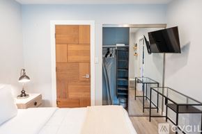 Los Angeles house for rent - A bedroom with a bed, a nightstand with a lamp, a wooden door, a staircase, a glass railing, and a flat-screen TV mounted on the wall.