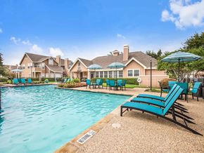 Irving apartment for rent - a swimming pool with blue chairs and umbrellas in front of a house