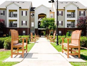 Starkville apartment for rent - an empty sidewalk with wooden chairs in front of an apartment complex