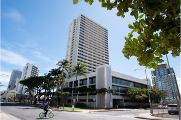 Honolulu apartment for rent - A tall white building with a lot of windows is in the middle of a street.