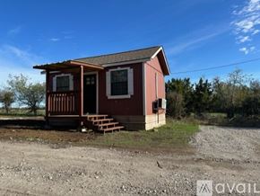 Hillsboro apartment for rent - A small red house with a porch is situated in a gravel area with trees in the background.