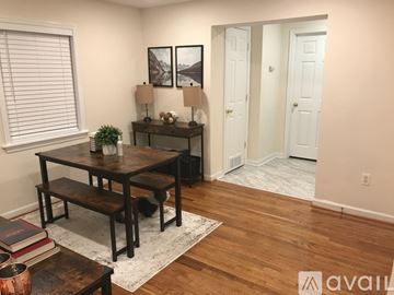 College Park apartment for rent - A living room with a wooden table and bench, two lamps, a potted plant, and two framed pictures on the wall.