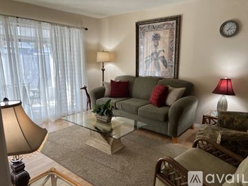 Sarasota condo for rent - A living room with a grey couch, a glass coffee table, and a painting on the wall.