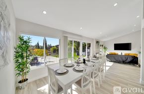 Los Angeles house for rent - A dining room with a white table and chairs, a television, and a view of the outdoors through large windows.