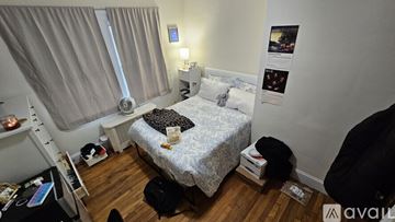 Boston house for rent - A small bedroom with a bed, a window with curtains, a nightstand with a lamp, and a wall with pictures and posters.