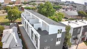 Dallas townhouse for rent - A modern building with a grey and white exterior is surrounded by trees and other buildings.