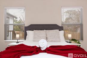 San Antonio house for rent - A bed with a red blanket and a white pillow is in the foreground with a window showing a view of a building in the background.