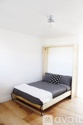 Denver apartment for rent - A bed with a grey pillow and a white sheet is in a room with wooden floors.