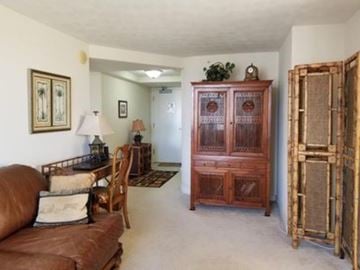 Honolulu condo for rent - A brown leather couch sits in a living room with a wooden cabinet and a chair.