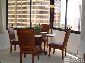 Honolulu condo for rent - A brown wooden table with four chairs in front of a window with a view of a building.