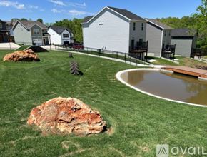 Waynesville apartment for rent - A large rock sits in the middle of a grassy area with a house and a pond in the background.