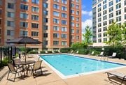 Alexandria apartment for rent - A pool surrounded by chairs and umbrellas in front of a brick building.