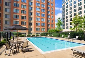 Alexandria apartment for rent - A pool surrounded by chairs and umbrellas in front of a brick building.