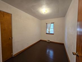 Gary house for rent - A room with a brown floor and a window with white curtains.