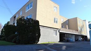 Victoria apartment for rent - A large beige building with a parking lot in front.