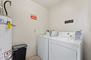 Burbank apartment for rent - A small laundry room with a washer and dryer and a trash can.