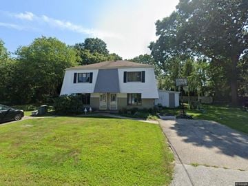 Narragansett apartment for rent - A white house with a grey roof is surrounded by greenery.